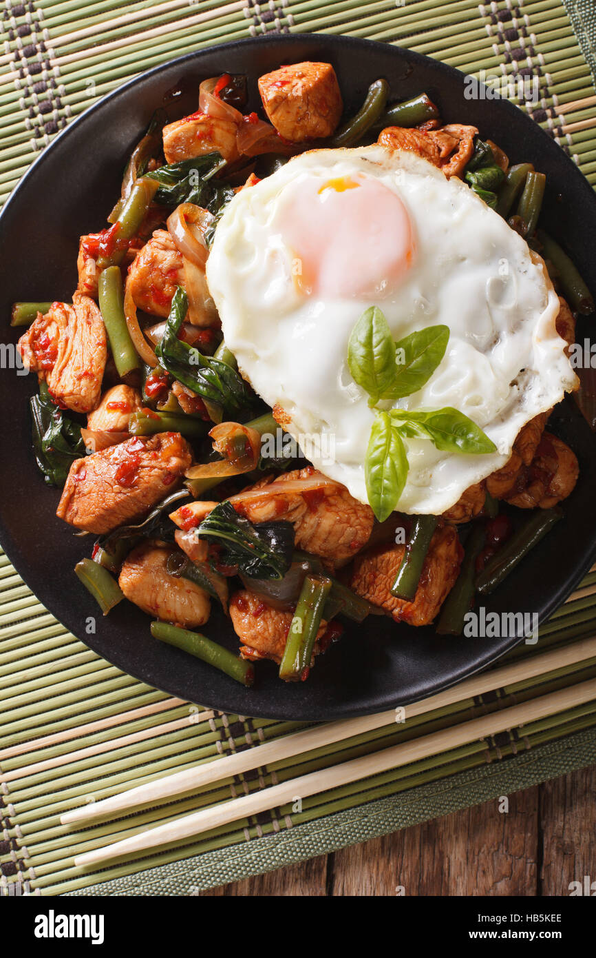 Stir-Fry pollo con basilico, fagioli verdi e un uovo fritto su una piastra di close-up. vista verticale da sopra Foto Stock