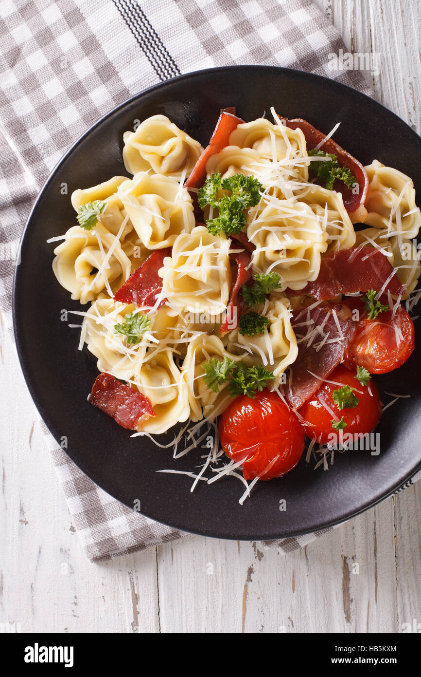 Italian tortellini con prosciutto, pomodori e parmigiano close-up su una piastra. vista verticale da sopra Foto Stock