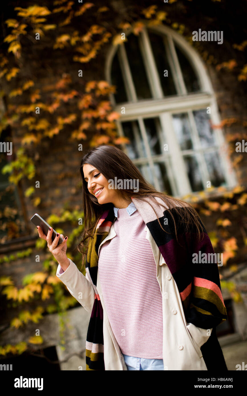 Giovane donna con un cellulare in autunno per esterno Foto Stock