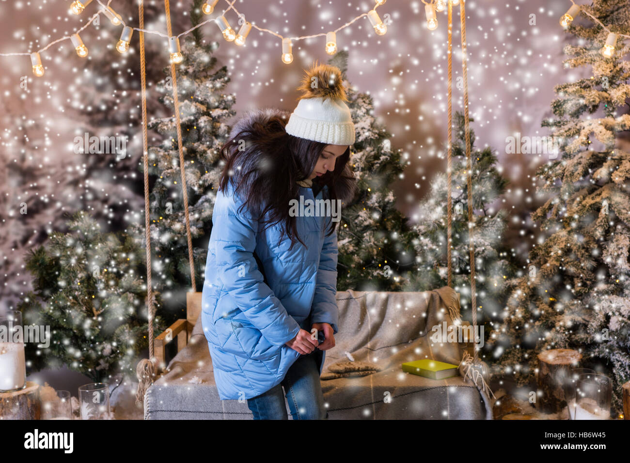 Carino donna abbottonata fino her blue Down Jacket e in piedi vicino a swing con una coperta sotto le torce elettriche in una coperta di neve park, indossare caldo k di lana Foto Stock