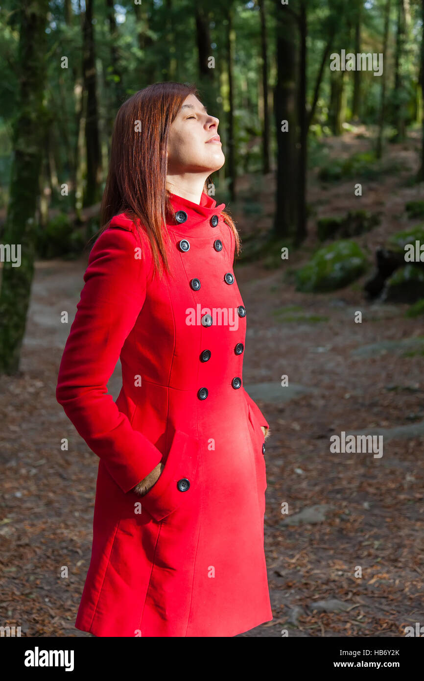 Donna godendo il calore del sole d'inverno su una foresta che indossa un soprabito rosso Foto Stock