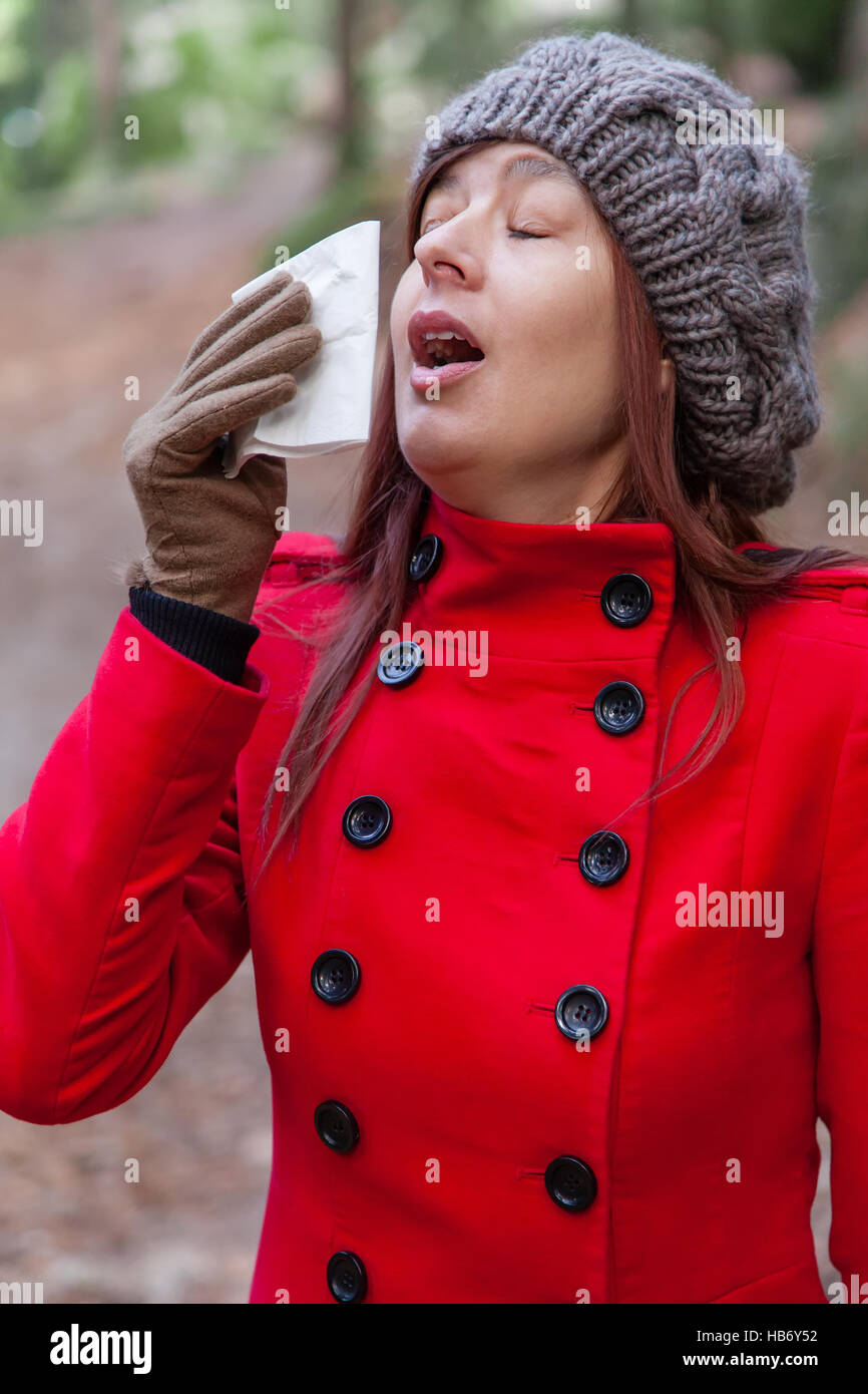 Giovane donna che soffre di un raffreddore, influenza o allergie starnuti su un fazzoletto di carta durante il periodo invernale Foto Stock