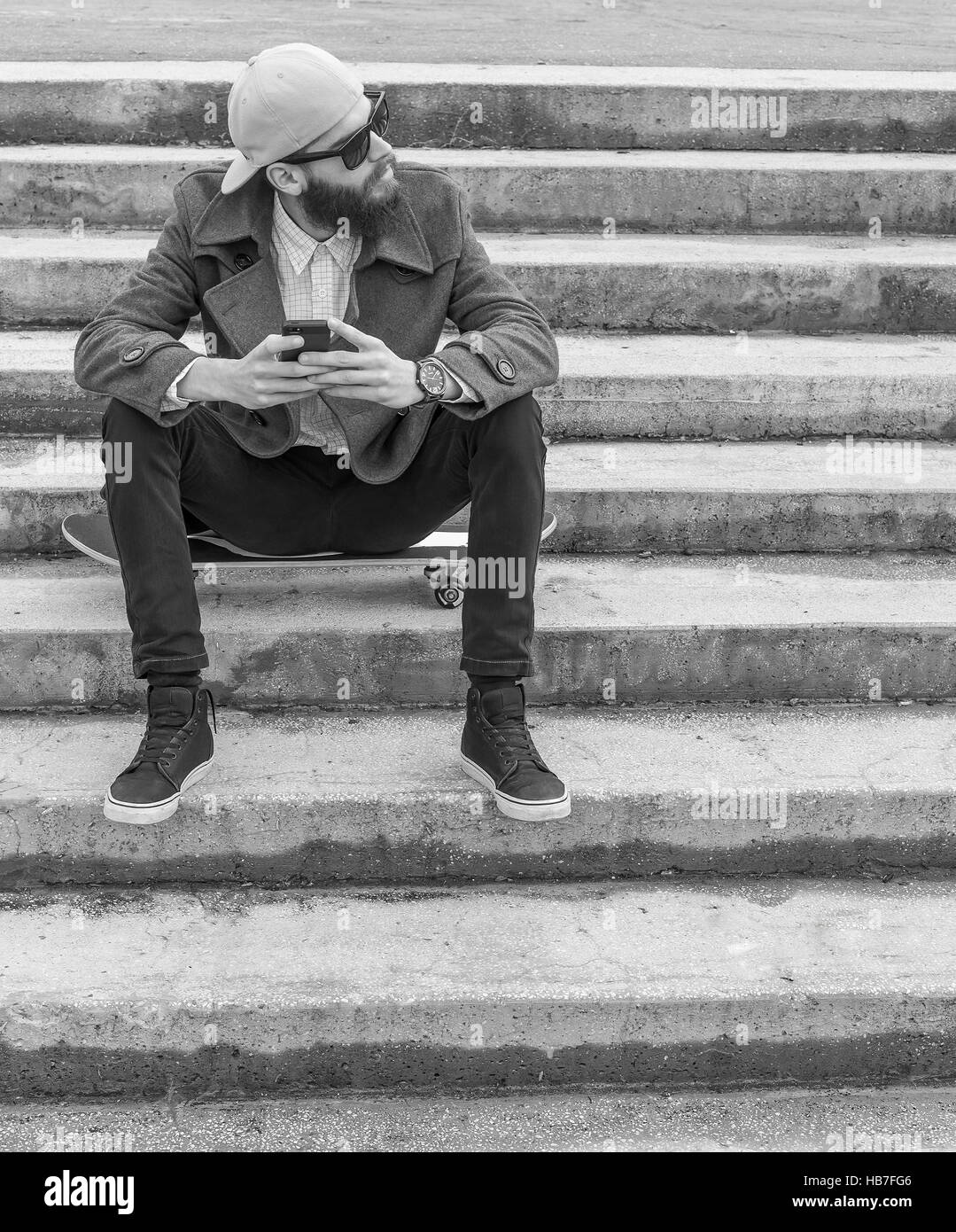 Giovane uomo con lo skateboard in possesso di un telefono cellulare. Foto Stock