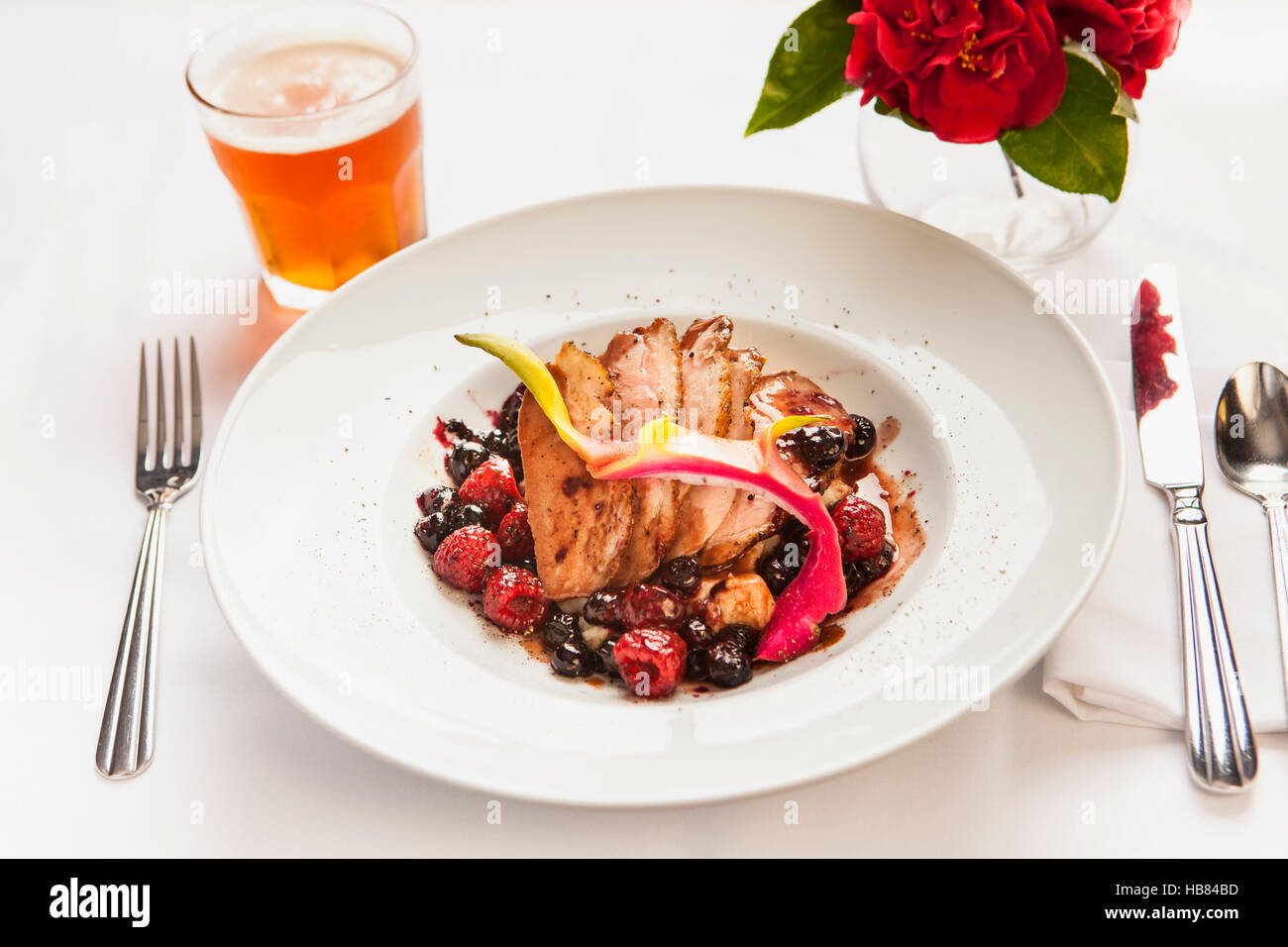 Arrosto di maiale con salsa di frutti di bosco e un bicchiere di birra Foto Stock