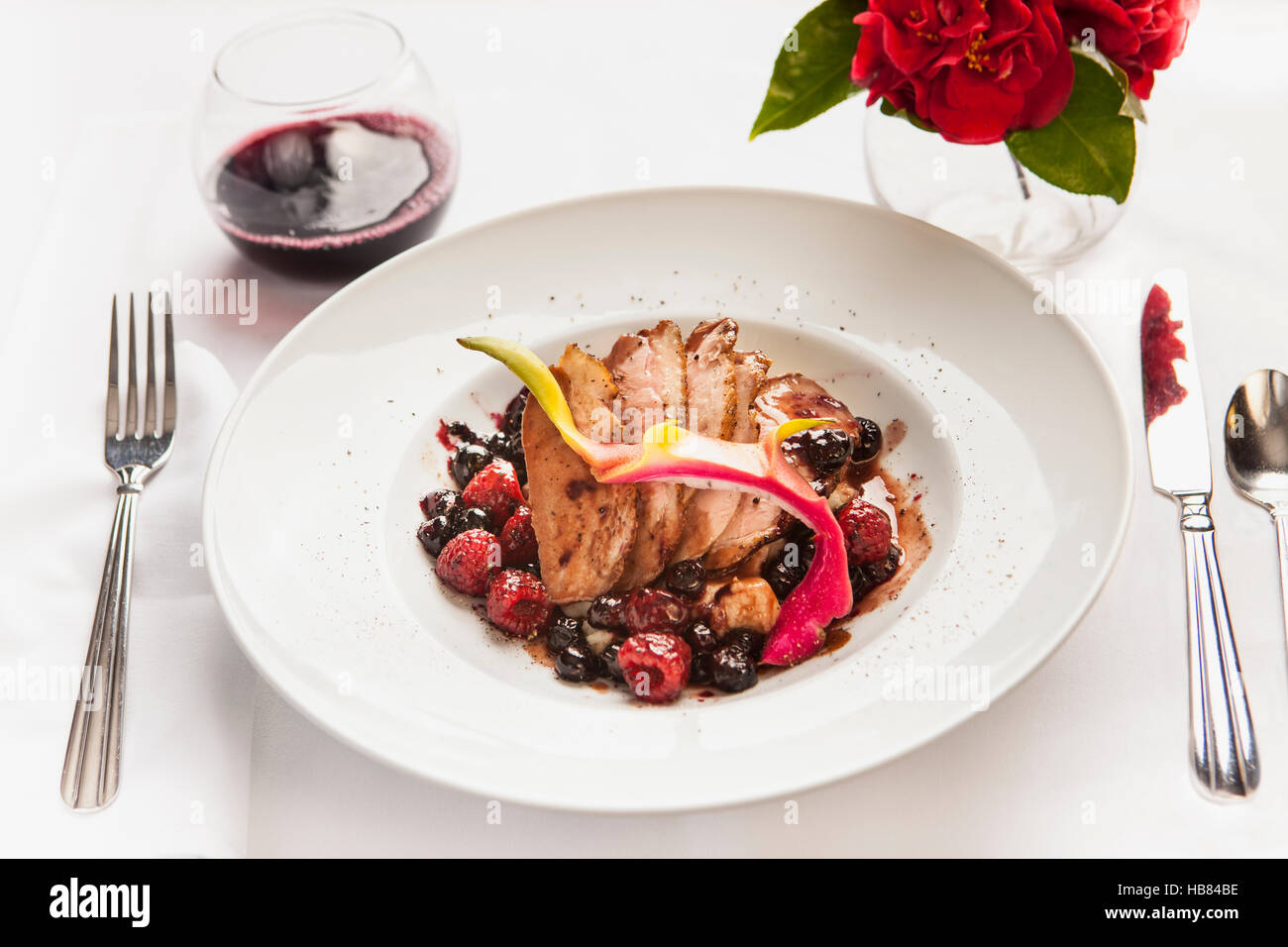 Arrosto di maiale con salsa di frutti di bosco e un bicchiere di pinot nero vino Foto Stock