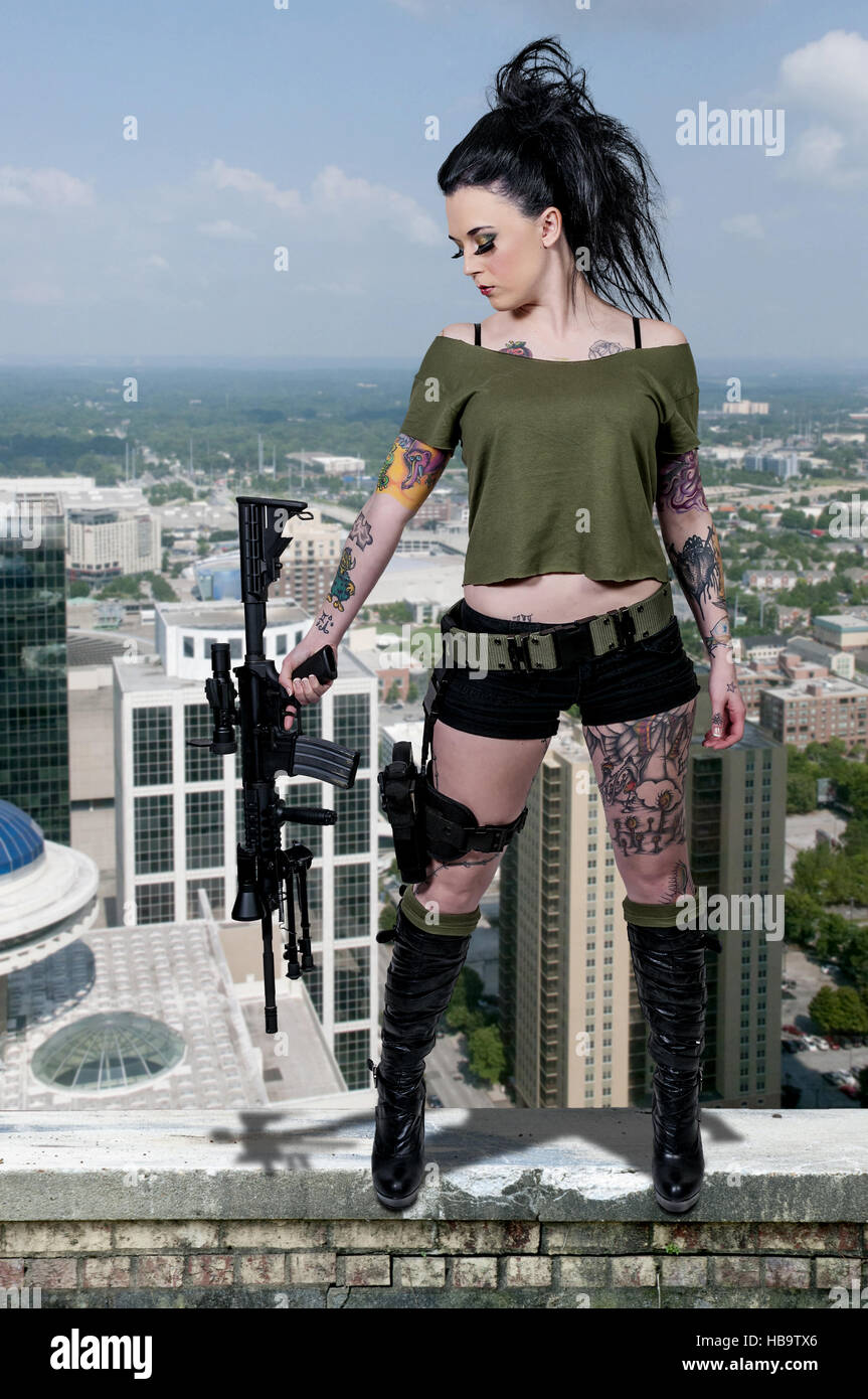 La donna tatuata con il fucile di assalto e pistola Foto Stock