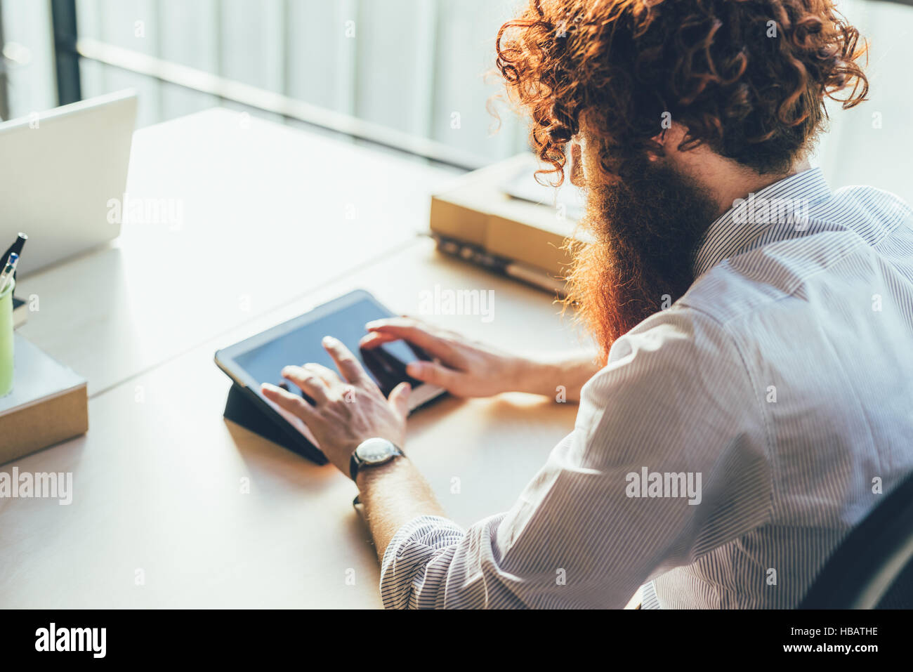 Giovane maschio hipster con i capelli rossi e la barba con tavoletta digitale touchscreen a scrivania Foto Stock