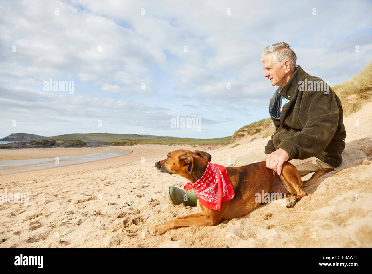 Uomo e cane seduto sulla spiaggia, Constantine Bay, Cornwall, Regno Unito Foto Stock