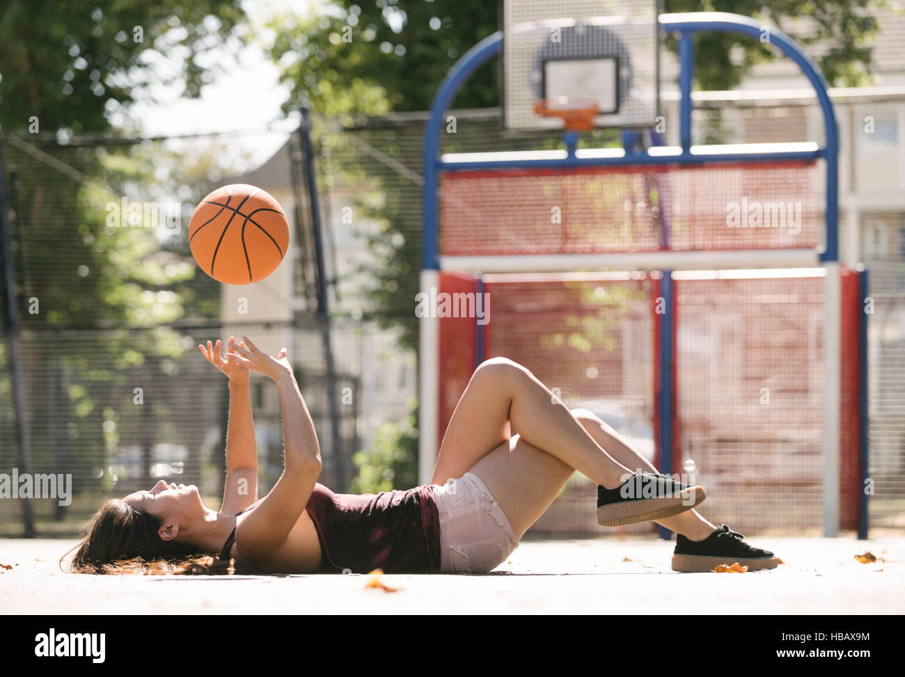 Giovane donna giacente sul campo da basket gettando la sfera Foto Stock