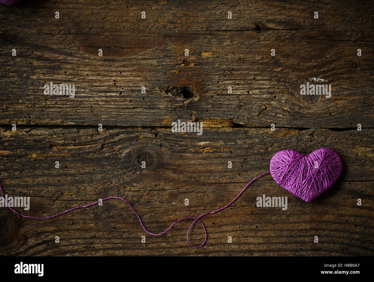 Cuore viola con una palla di filo sul vecchio squallido sfondo di legno. Immagine del giorno di San Valentino Foto Stock
