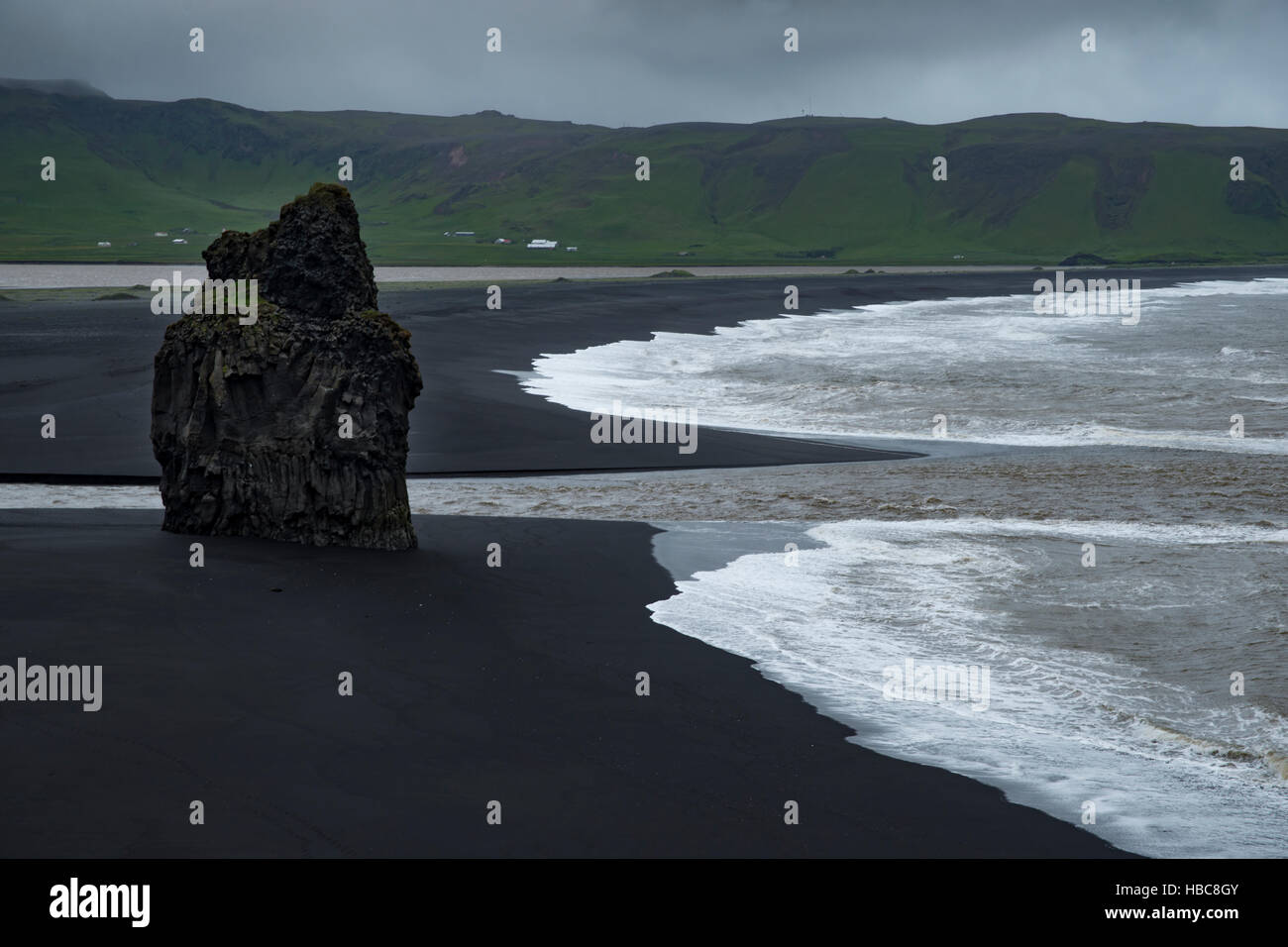 White onde si infrangono contro lonely roccia basaltica e nero spiaggia vulcanica Foto Stock