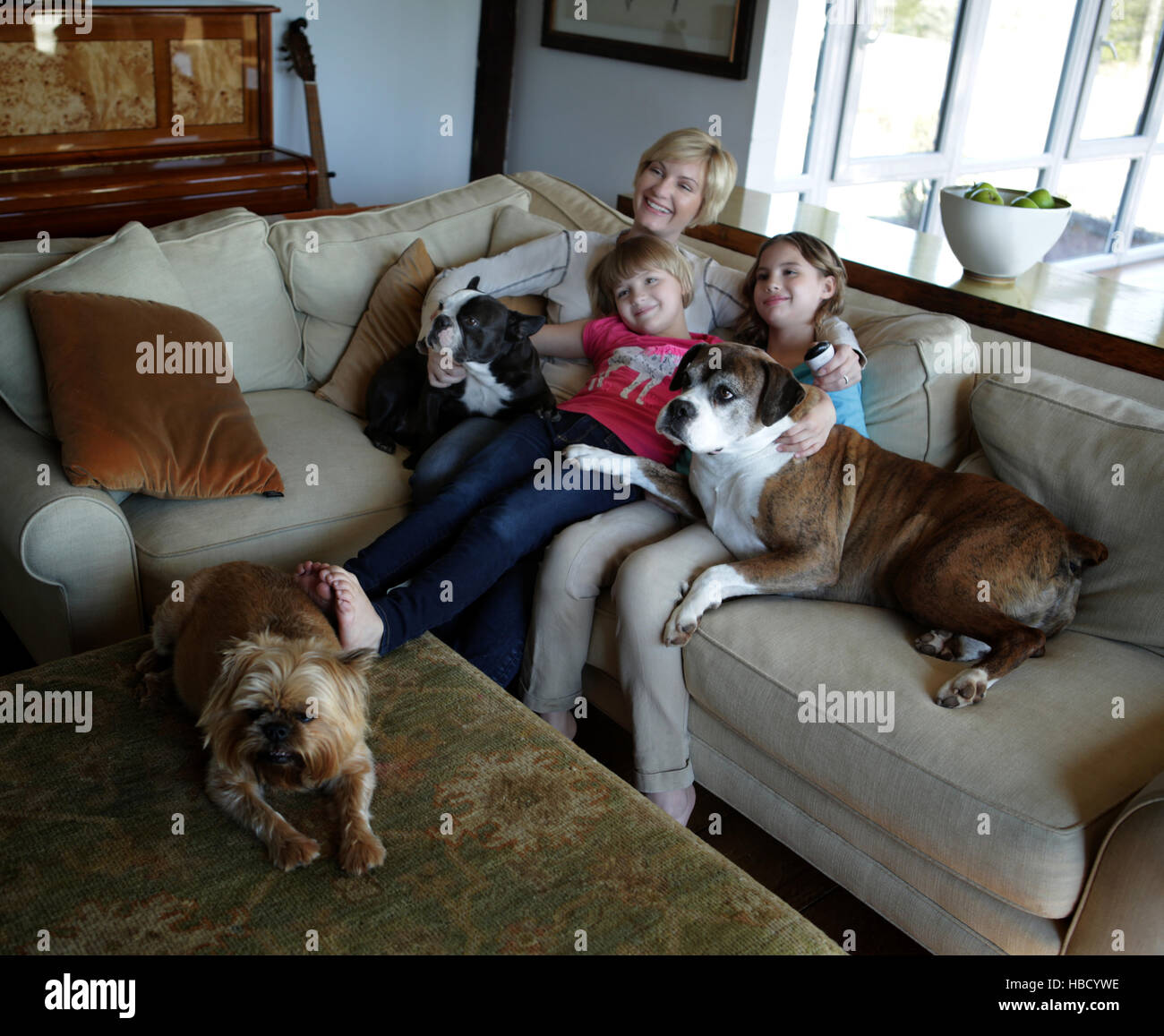 La madre e le figlie seduto sul divano con animali domestici cani, guardando la TV insieme Foto Stock