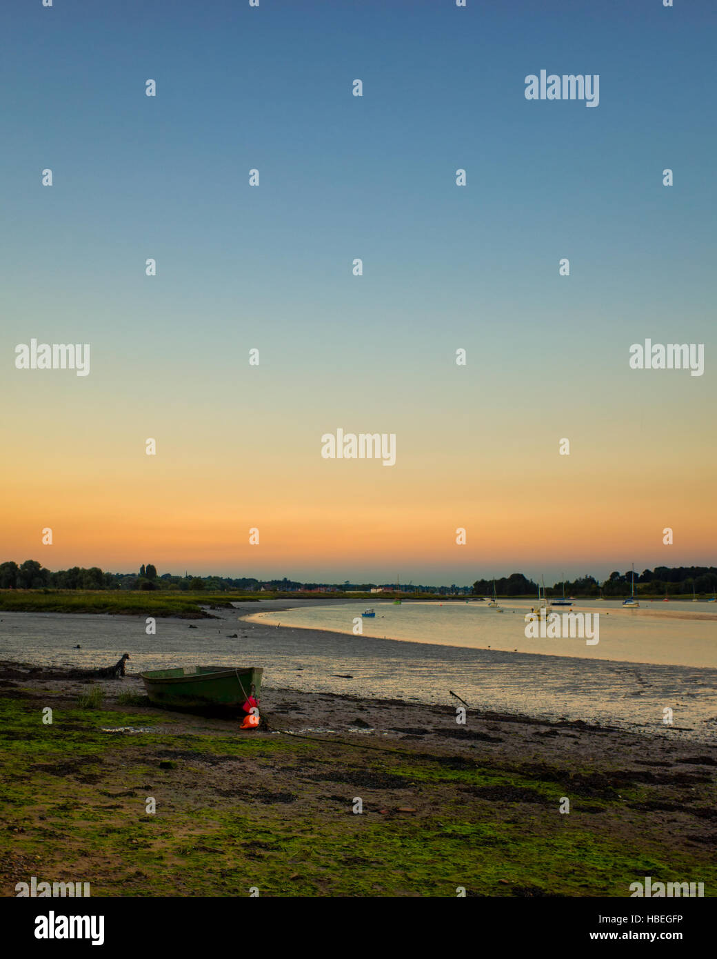 Fiume Deben Woodbridge, Inghilterra. Una piccola barca a terra sulle rive del fiume Deben nel crepuscolo. Il cielo è blu con arancia appena sopra l'orizzonte, che si riflette sull'acqua. Questa fotografia è stata presa solo dopo il tramonto che fa una bella luce morbida durante il crepuscolo precoce. Foto Stock