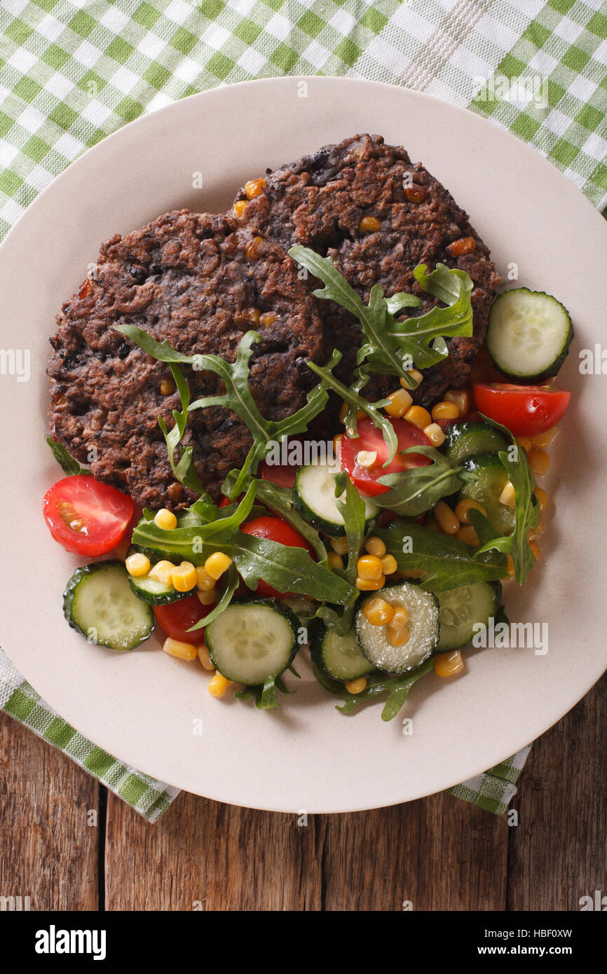 Cibo vegetariano: chicco nero hamburger e insalata di verdure fresche close-up su una piastra. vista verticale da sopra Foto Stock