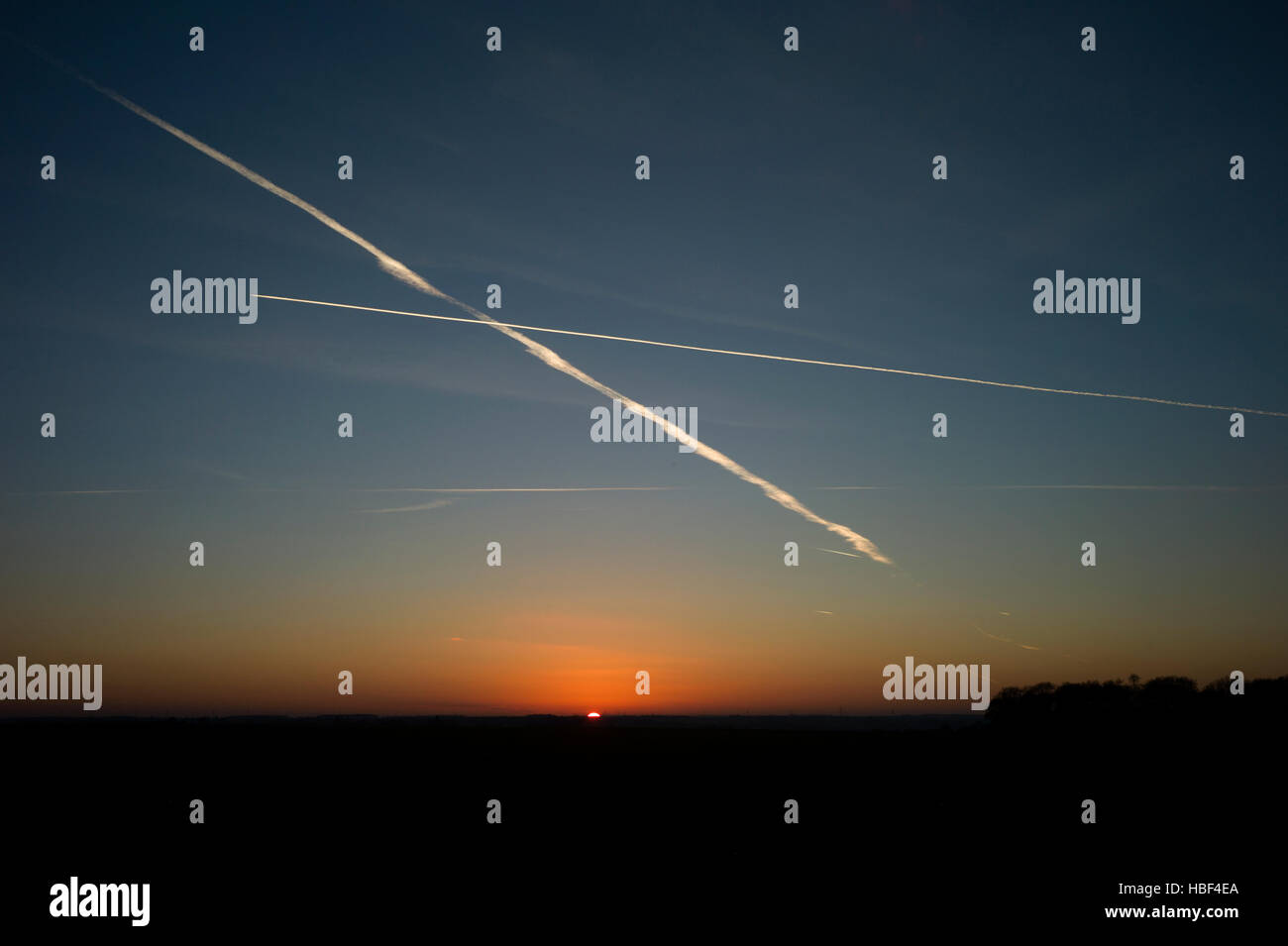 Piano di getto le scie di condensazione sopra Essex Inghilterra al tramonto quando il sole tramonta ad ovest. Dic 2016 Foto Stock
