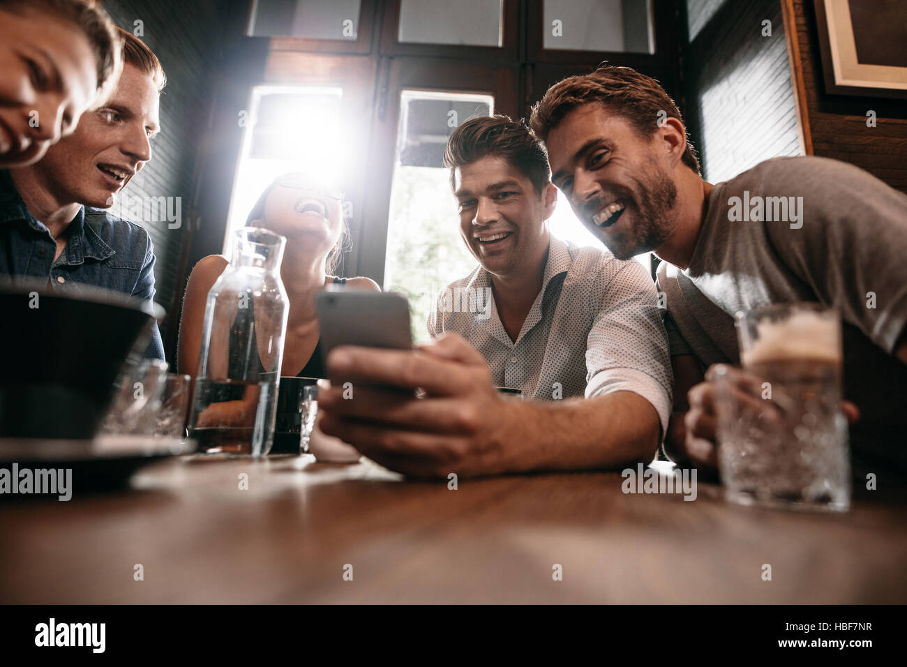 Gruppo di amici seduti insieme in una caffetteria guardando smart phone e sorridente. Giovane ragazzo che mostra qualcosa ai suoi amici sul suo telefono cellulare. Foto Stock