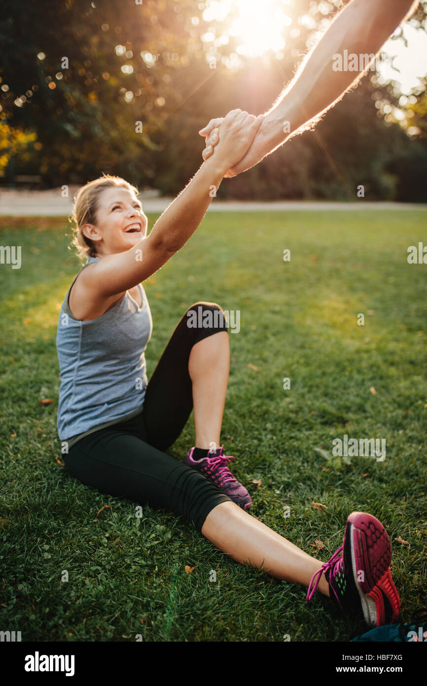 Colpo di uomo donna aiuta ad alzarsi in piedi. Sano giovane coppia al park che esercitano insieme. Foto Stock