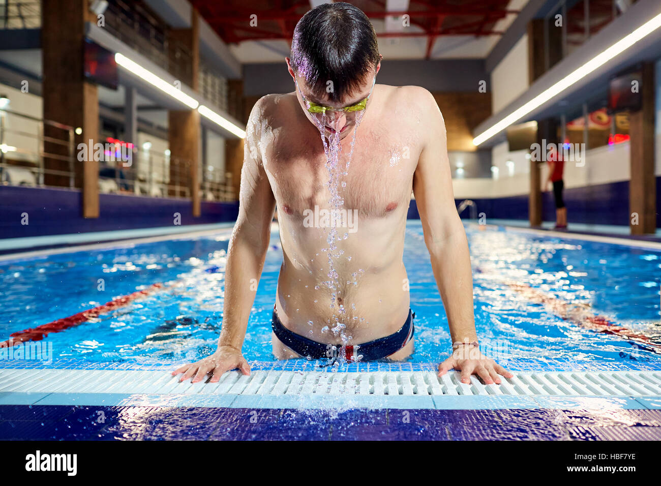 Nuotatore emerge dall'acqua piscina con schizzi in ambienti chiusi. Foto Stock