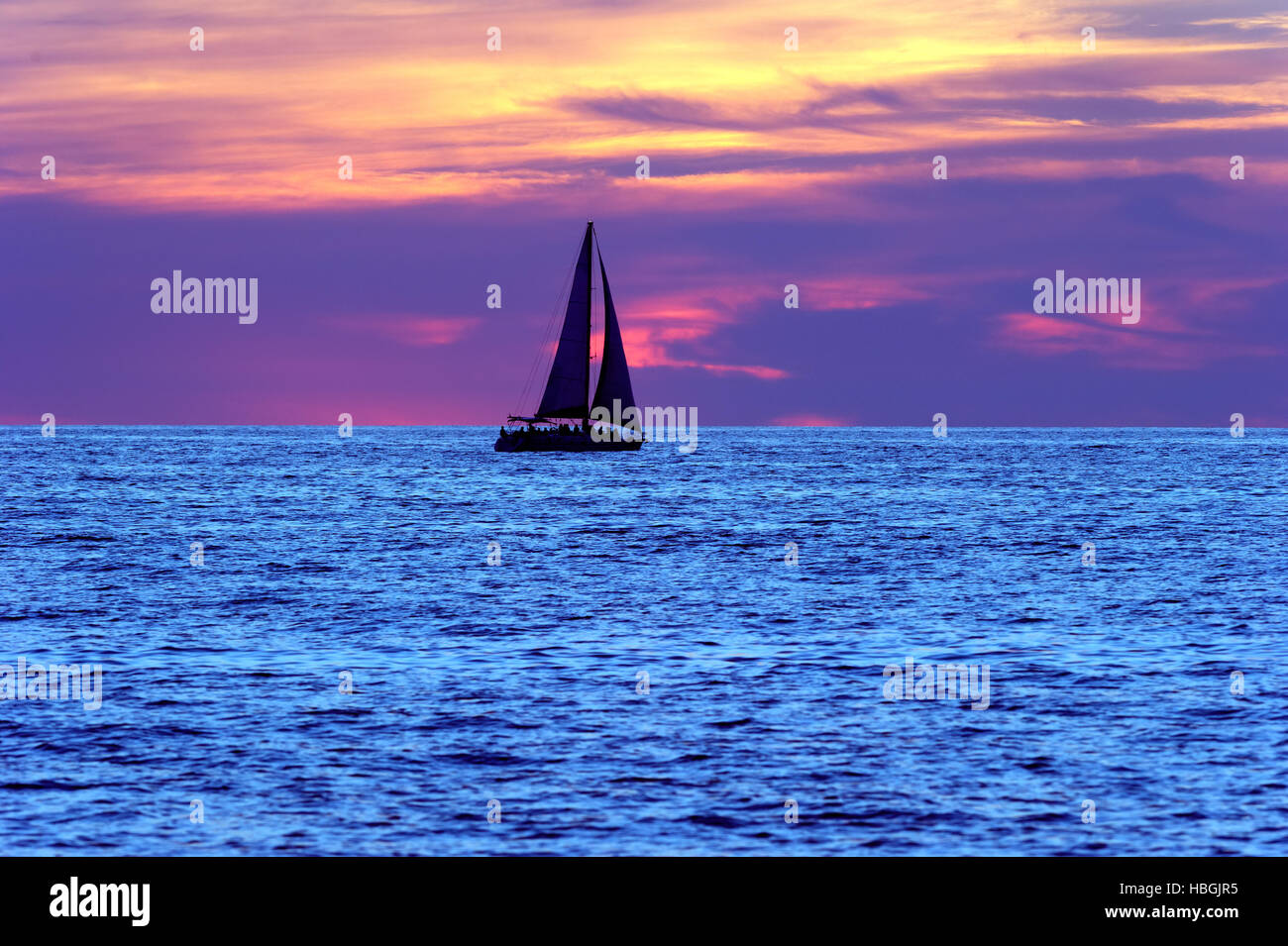 Barca a vela sunset silhouette è una barca a vela vela lungo l'acqua con un variopinto cielo notturno in background. Foto Stock