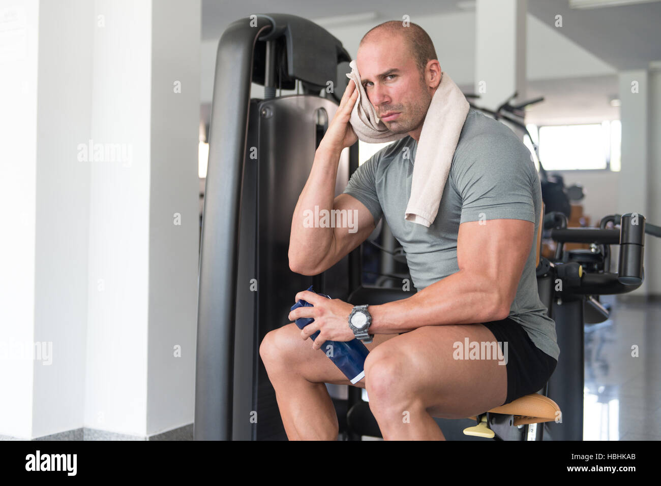 Uomo muscolare riposo dopo esercizio fisico e asciuga il sudore con un asciugamano Foto Stock