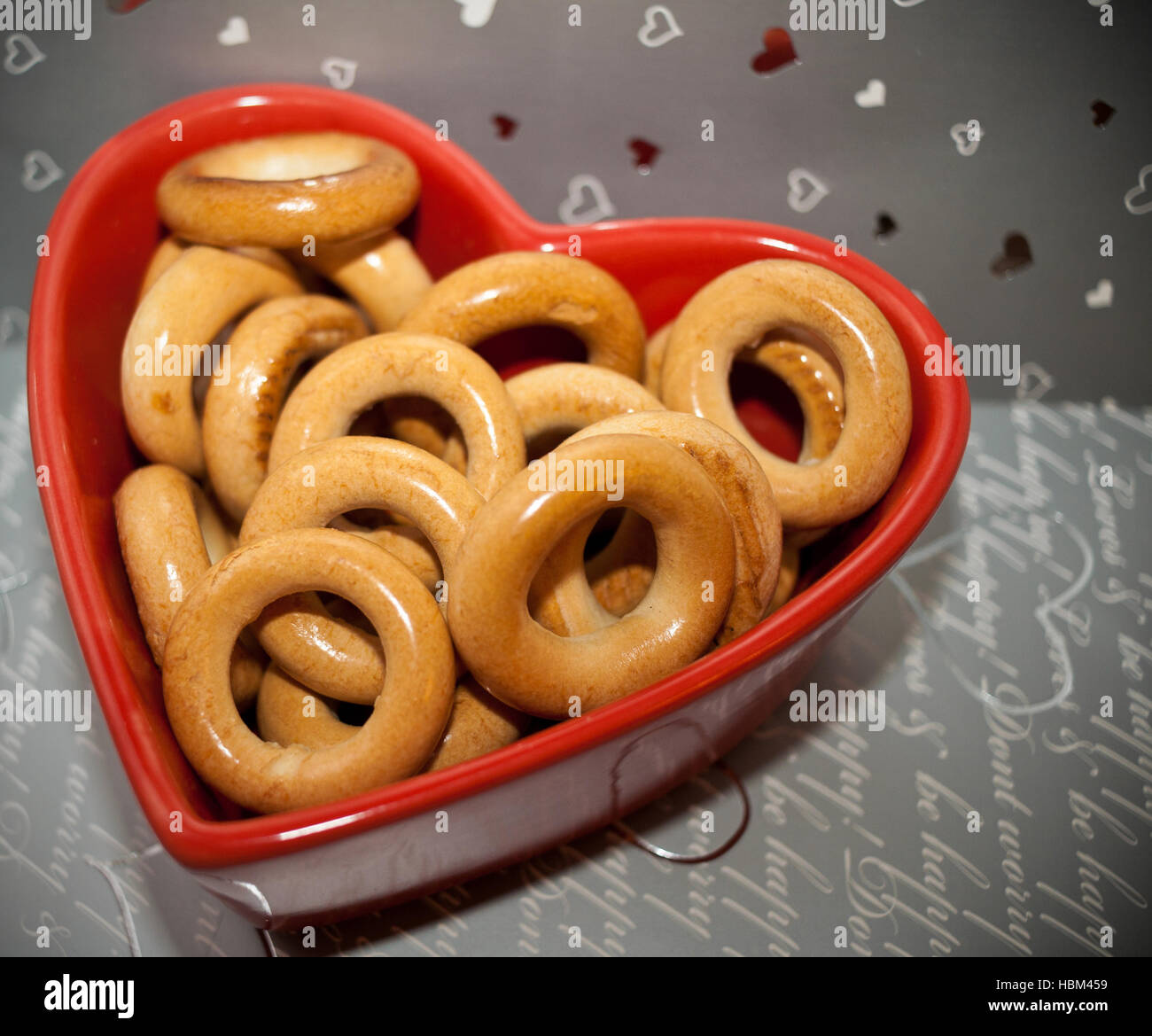 Bagel sulla targhetta rossa a forma di cuore su uno sfondo grigio. Foto Stock