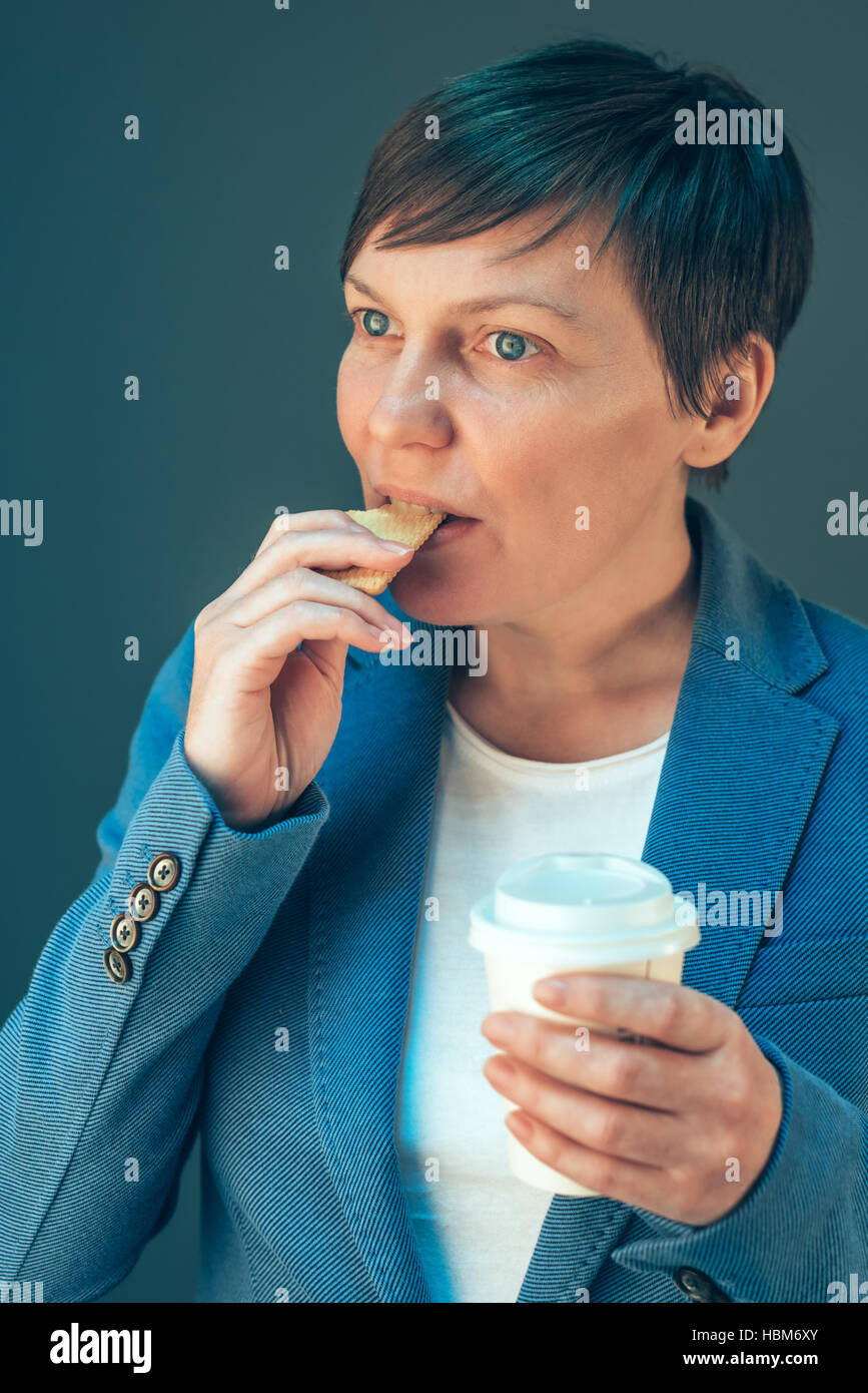 Imprenditrice mangiare cookie su una pausa, dieta e snack veloce sul lavoro Foto Stock