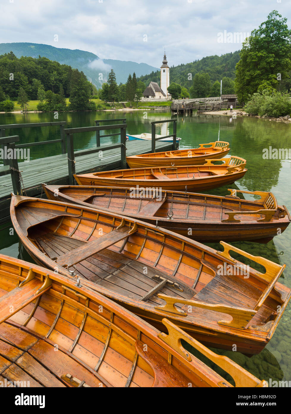 Il lago di Bohinj (Bohinjsko jezero), il Parco Nazionale del Triglav, Alta Carniola, Slovenia. Barche a remi a noleggio. La chiesa di San Giovanni (Cerkev sv Janeza) a R Foto Stock