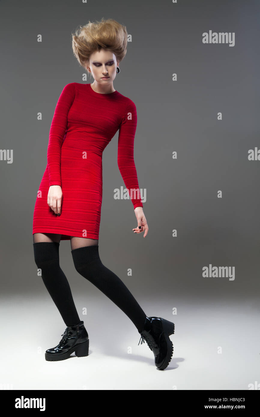 Giovani modello femminile in abito rosso, nero di scorte e stivali con acconciatura in posa di studio. Foto Stock
