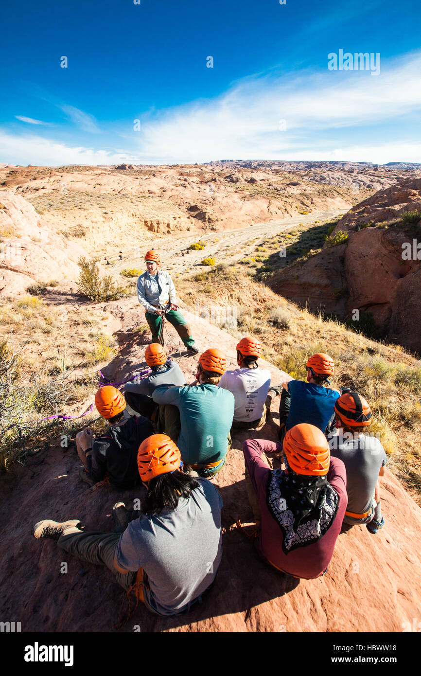 Una femmina di outdoor educatore insegna a un gruppo di studenti di sesso maschile come rappell nel deserto canyon dello Utah. Foto Stock