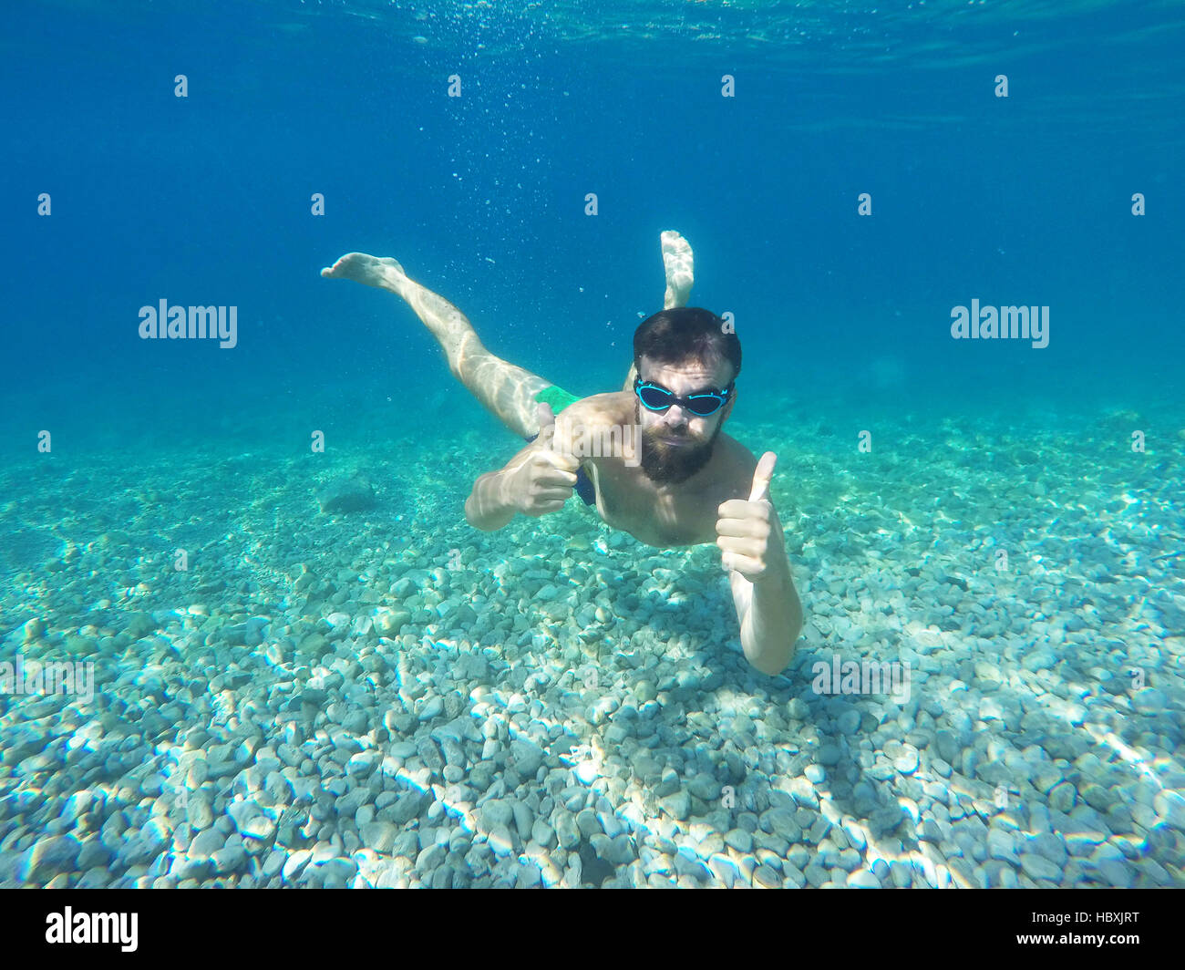 Barba Giovane Uomo con occhiali immersioni in acqua pulita azzurra con il pollice in alto Foto Stock