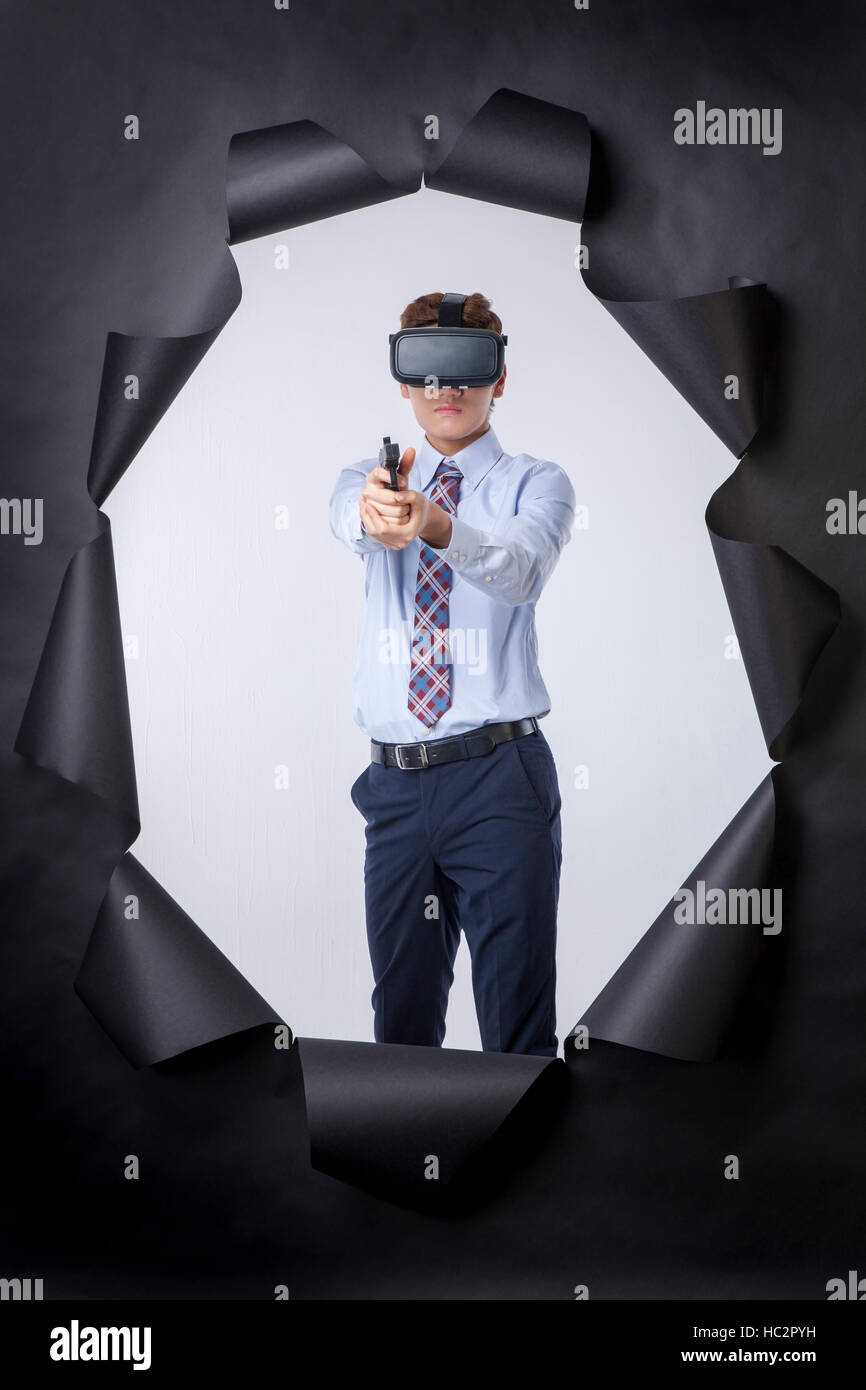 Giovane imprenditore indossando la realtà virtuale auricolare livellamento permanente di una pistola nel foro tornon carta nera Foto Stock
