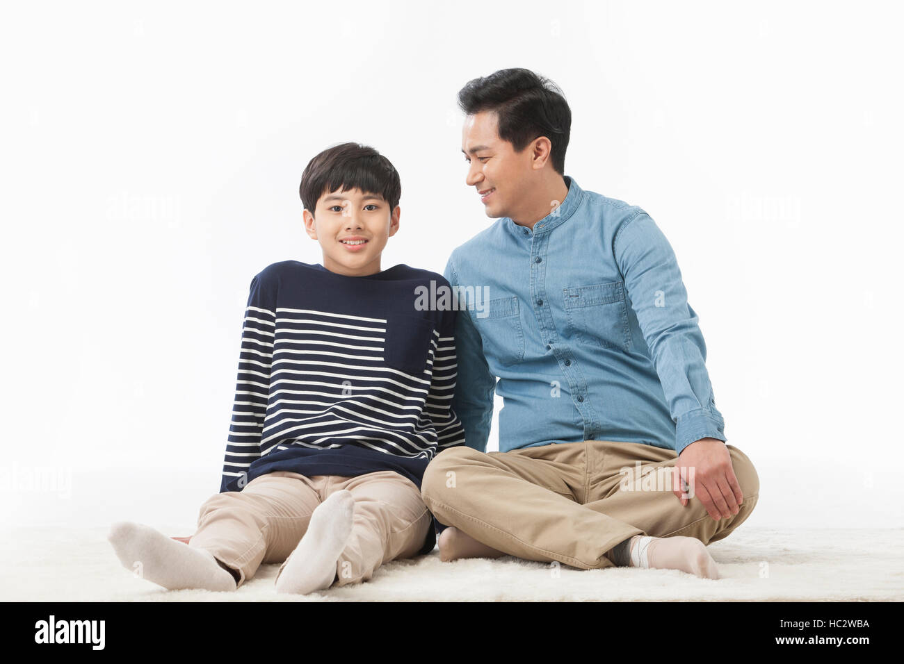 Sorridente padre e figlio adolescente seduto su un tappeto Foto Stock