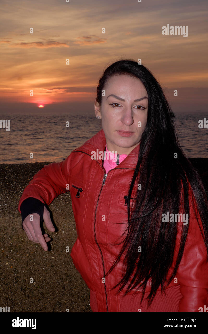 Femmina appoggiata contro un muro sul lungomare al tramonto a Southsea England Regno Unito Foto Stock