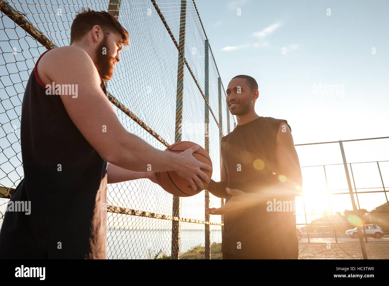 Giovane maschio uomo sportivo dando la pallacanestro al suo amico mentre in piedi presso il parco giochi Foto Stock