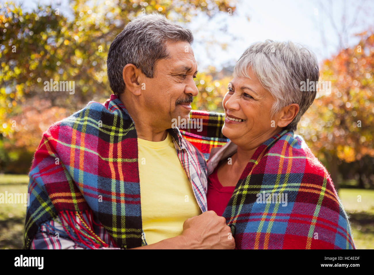 Coppia di anziani seduti su un banco a sorridere a ogni altro con una coperta Foto Stock