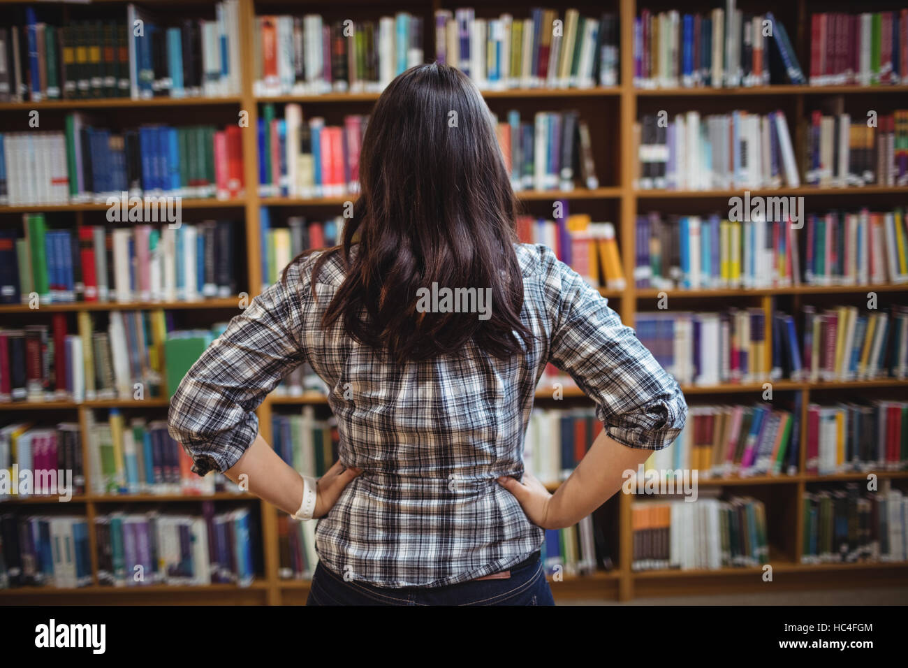 Vista posteriore della studentessa guardando i libri nel ripiano Foto Stock