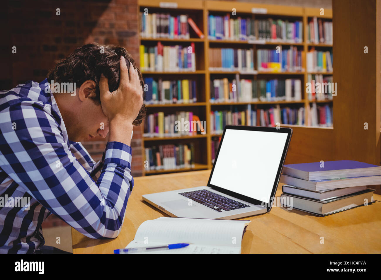 Premuto studente seduto nella libreria con il computer portatile Foto Stock