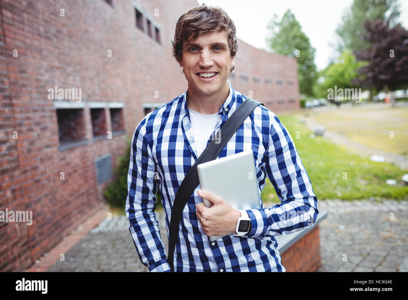 Sorridente permanente dello studente nel campus con tavoletta digitale Foto Stock