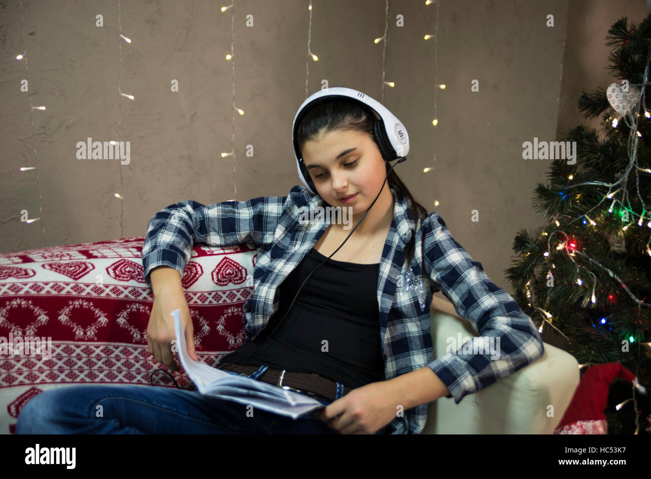 Teen ragazza seduta sul divano e ascoltare musica e divertirsi vicino all'albero di natale Foto Stock