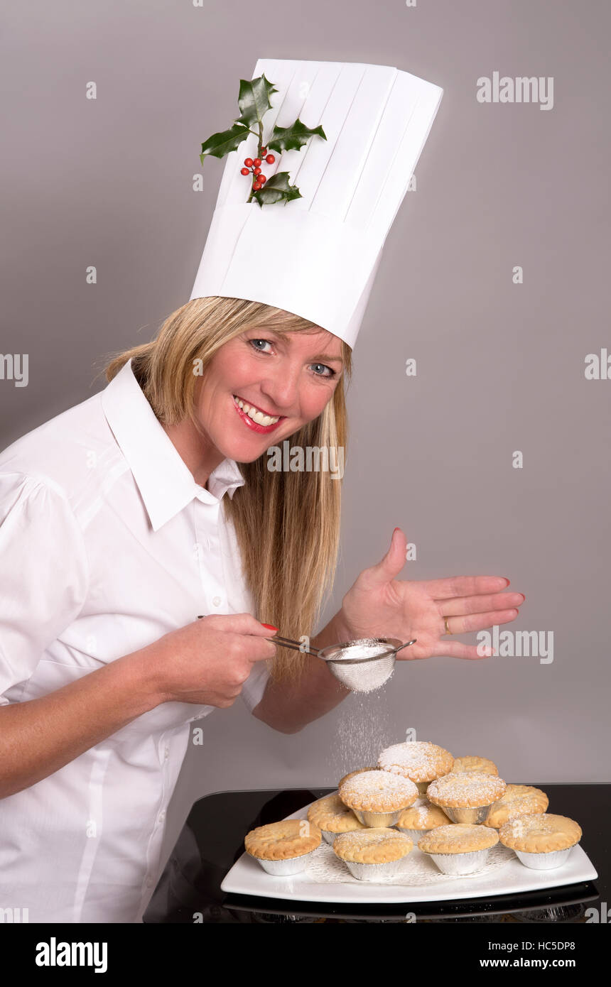 Lo chef con un rametto di agrifoglio nel suo hat applicazione di zucchero a velo per il tradizionale pasticci di carne macinata Foto Stock