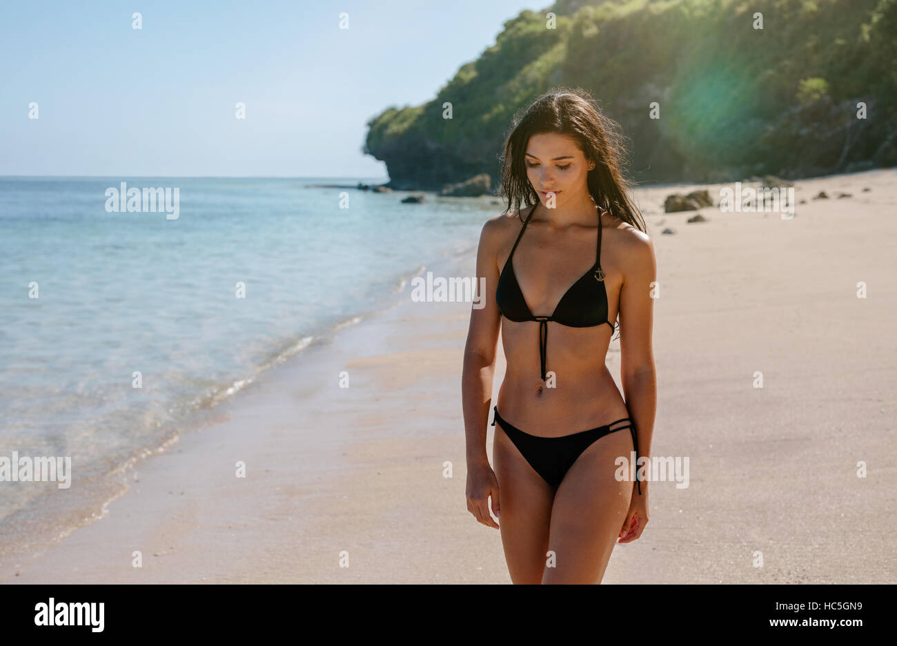 Colpo di attraente giovane donna in bikini di camminare sulla spiaggia. Modello femminile passeggiando lungo il litorale. Foto Stock