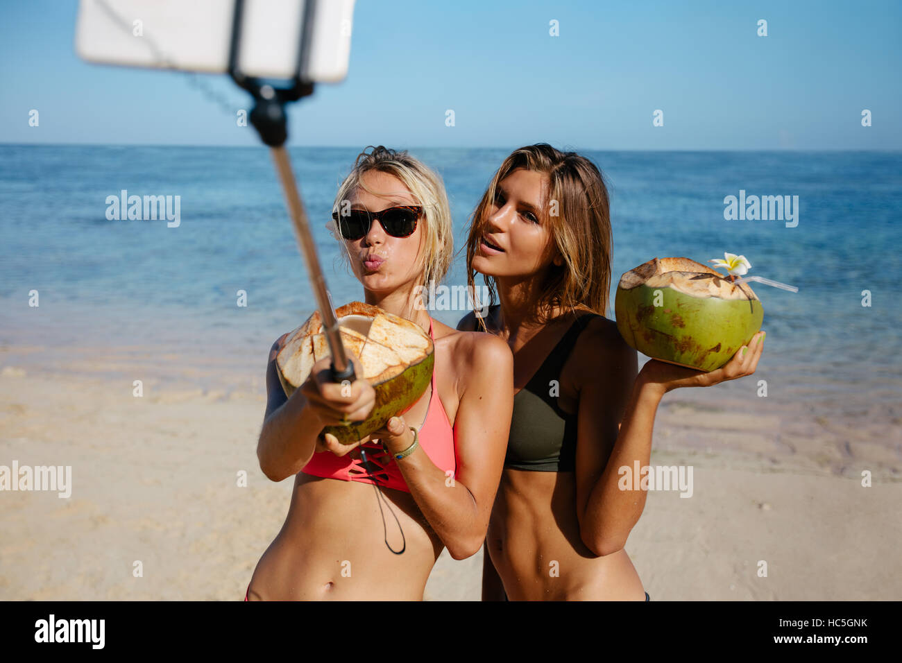 Due belle ragazze in bikini sulla spiaggia parlando autoritratto con smart phone su selfie stick. Amici di sesso femminile avente il divertimento sulla spiaggia con c Foto Stock