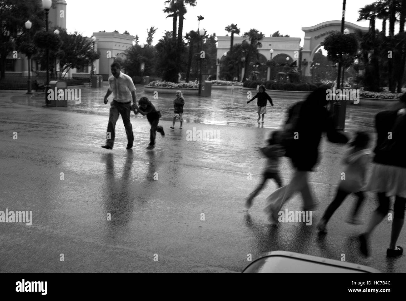Le persone che eseguono sotto la pioggia in un parco a tema Foto Stock