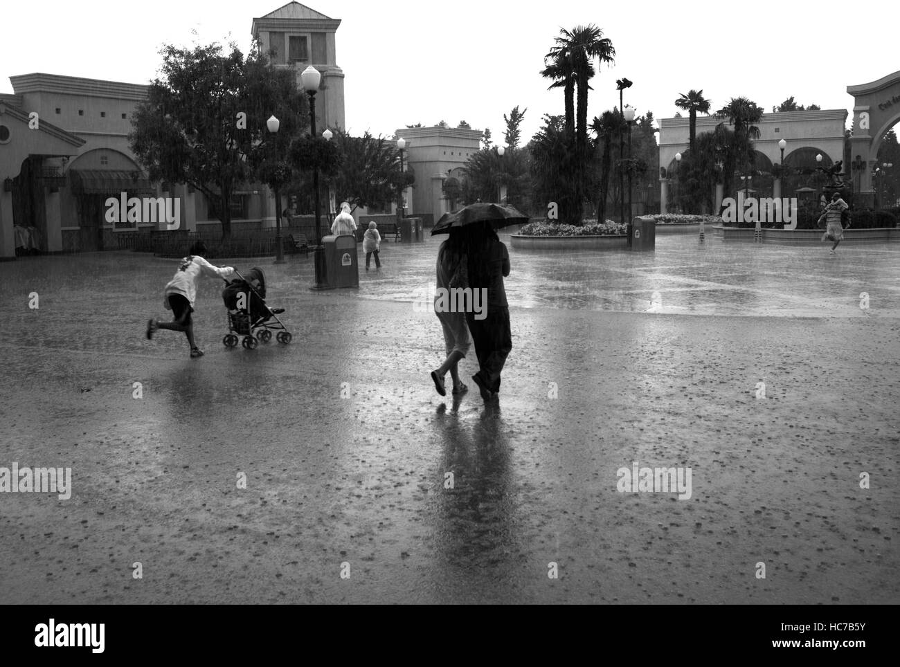 Le persone che eseguono sotto la pioggia in un parco a tema Foto Stock