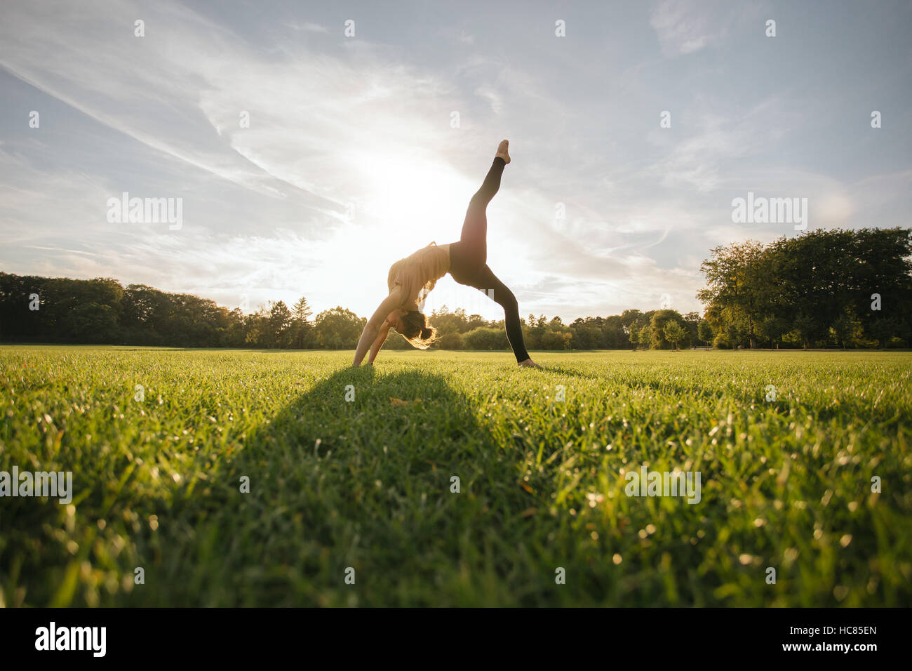 Sano giovane donna fare yoga all'esterno. Montare il giovane femmina facendo esercizio acrobatico nel parco. Foto Stock