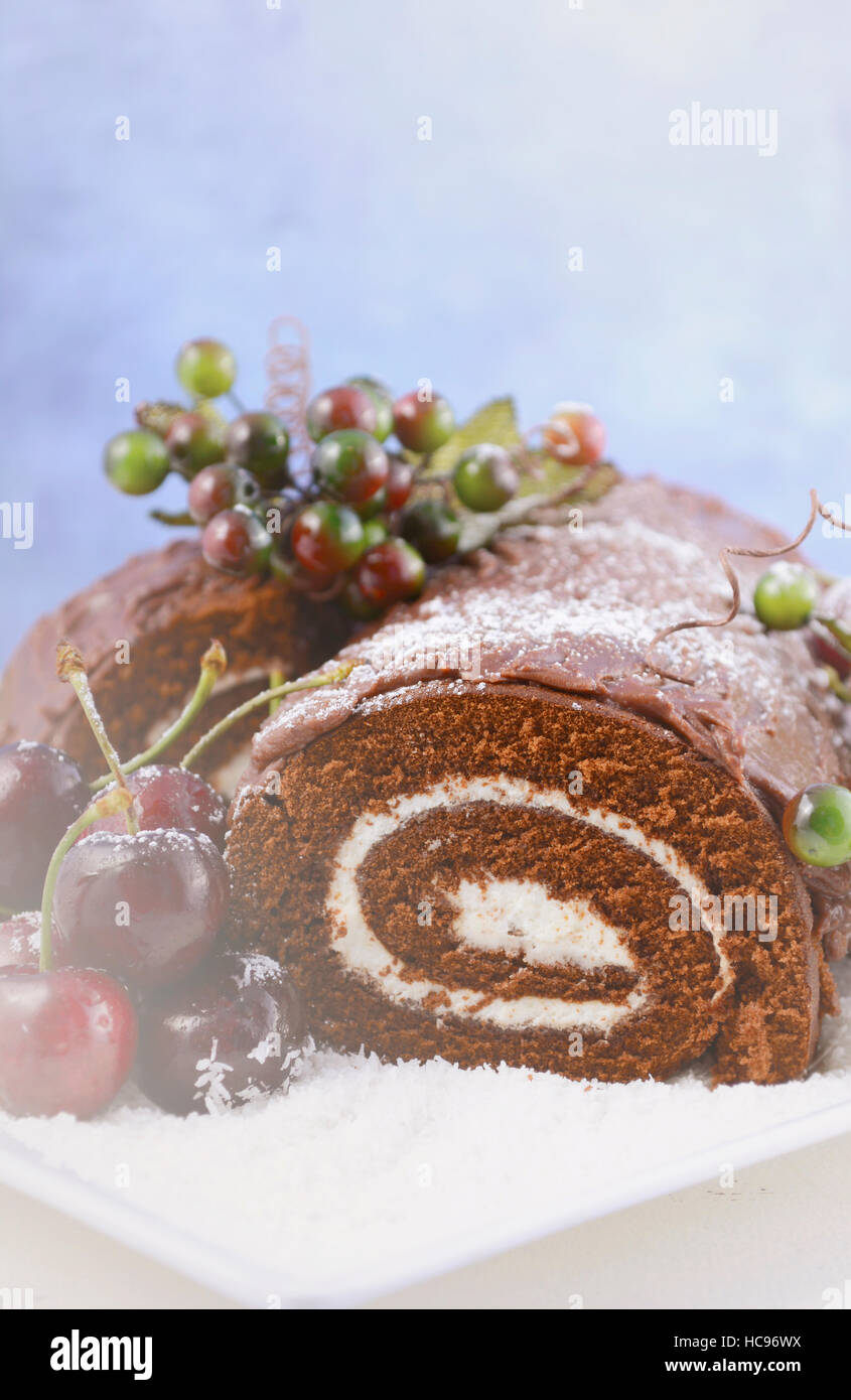 Natale Yule Log, Buche de Noel, torta al cioccolato con la diramazione, fresche Ciliege e festoso berry decorazioni su un bianco piatto di portata., con applicata Foto Stock