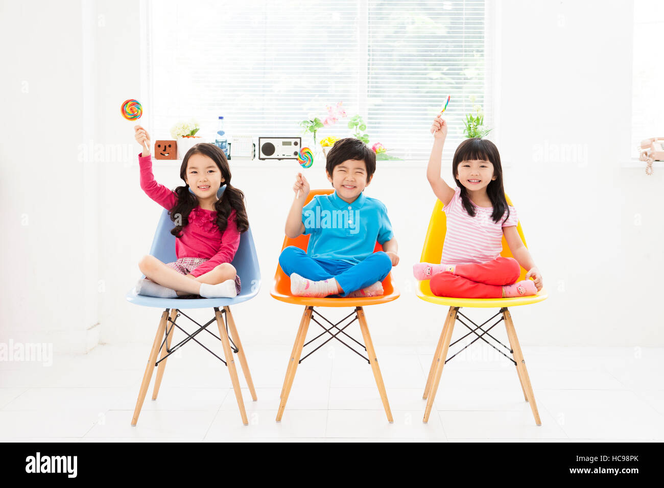 Tre bambini sorridenti con lollipop caramelle seduti su sedie Foto Stock