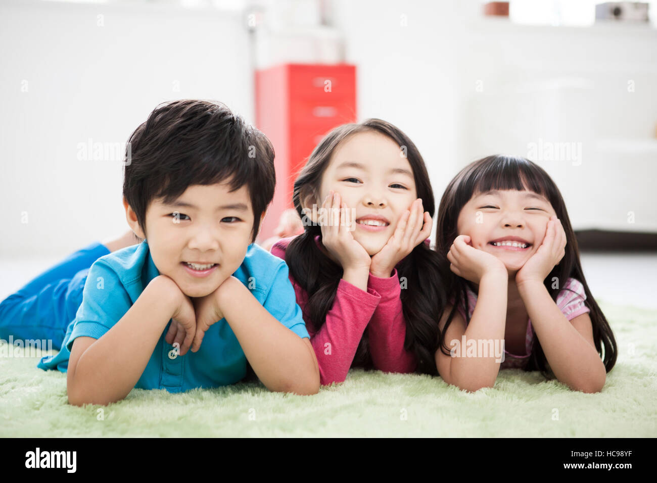 Ritratto di tre bambini sorridenti giacenti sia rivolto verso il basso e posizionando i menti in mani Foto Stock