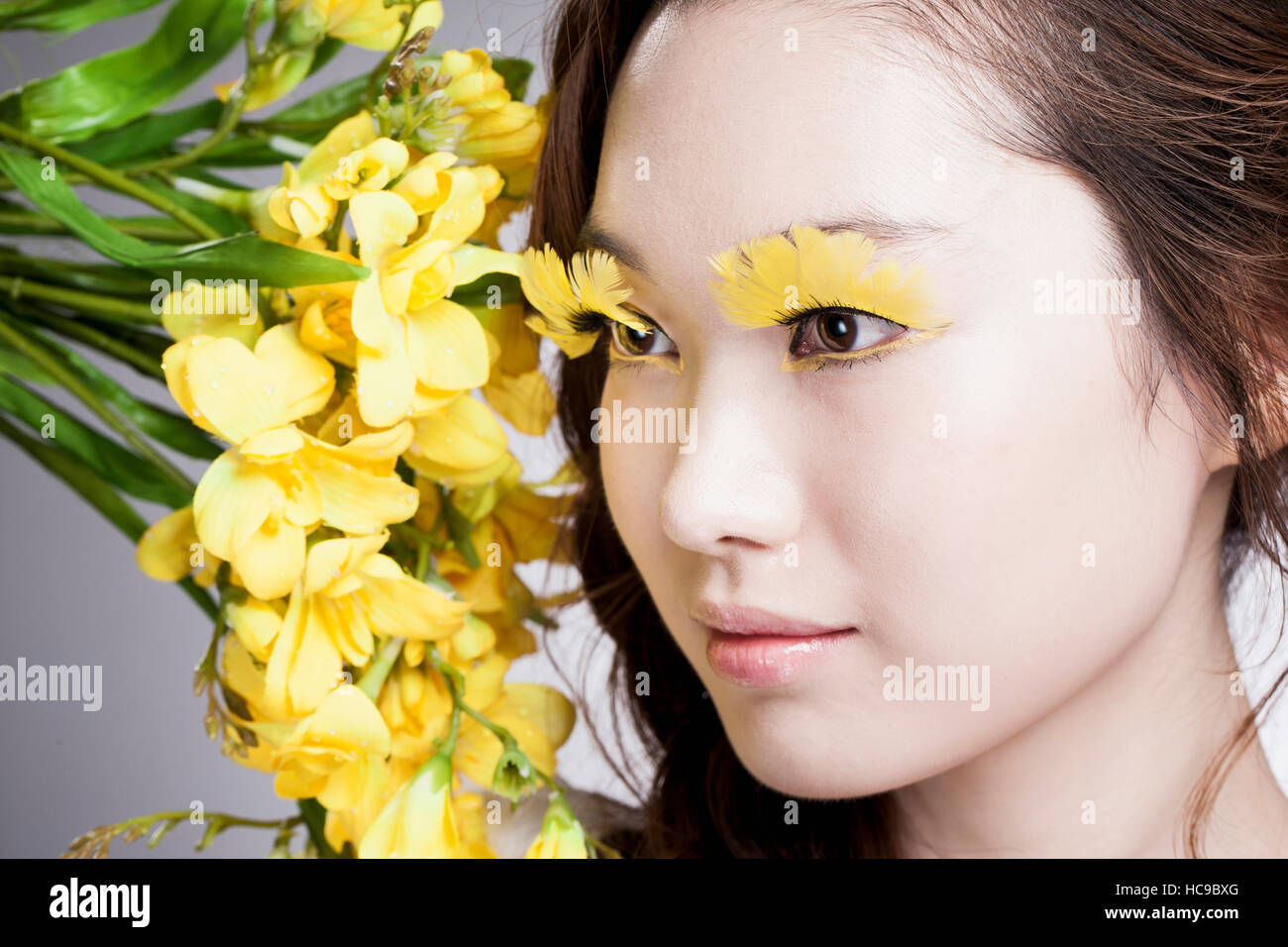 Vista laterale del giovane sorridente donna coreana con giallo ciglia finte e fiori Foto Stock