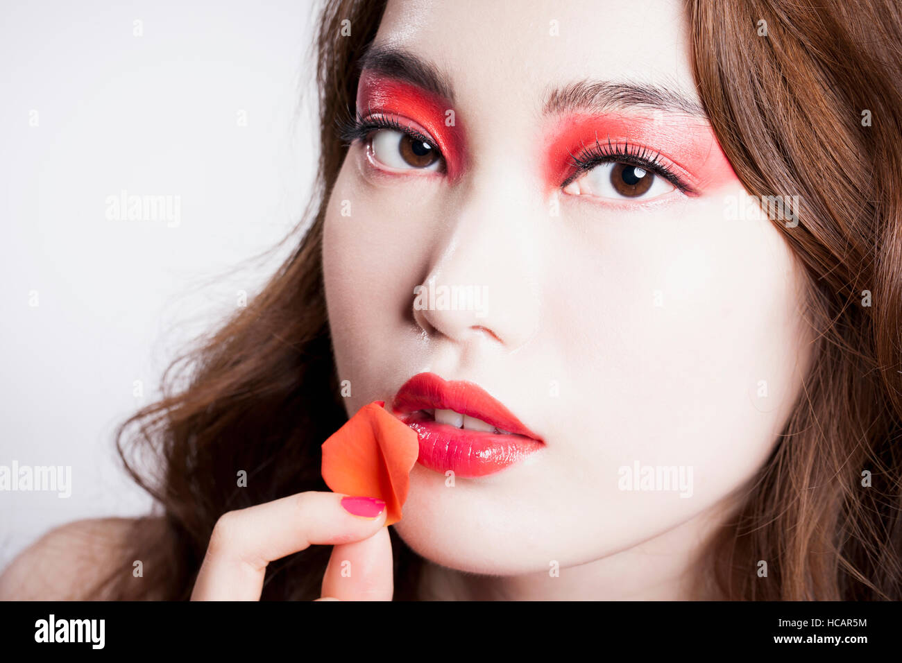 Ritratto di giovane donna coreana in red eye shadow e labbra rosse in posa con il petalo Foto Stock